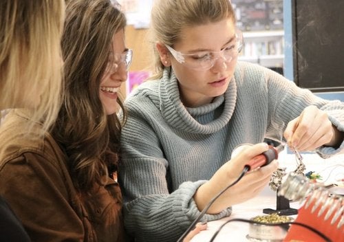 Two students wearing safety glasses soldering wires for a project